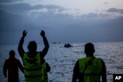 FILE - Volunteers guide an overcrowded dingy with refugees and migrants as it is approaches the beach after crossing a part of the Aegean sea from Turkey to the Greek island of Lesbos, Feb. 19, 2016.