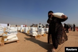 FILE - A displaced woman, who fled from Mosul because of Islamic State violence, carries food in Khazer refugee camp, east of Mosul, Iraq, Nov. 7, 2016.