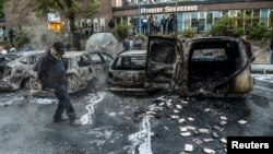 A bystander checks the debris around a row of burnt cars in the suburb of Rinkeby after youths rioted in several different suburbs around Stockholm, May 23, 2013.