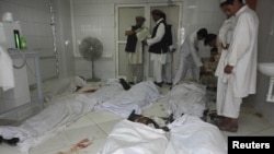 Afghan men stand over the bodies of a suicide bomb blast victims at a hospital in Khost province, June 20, 2012.