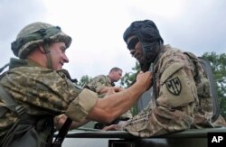 FILE - U.S. and Ukrainian servicemen talk during the opening ceremony for the Rapid Trident/Saber Guardian 2015 military exercises at the International Peacekeeping and Security Centre base outside Lviv, Ukraine, July 20, 2015.