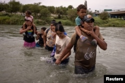 Orlando, migran dari Ekuador, menggendong rekan senegaranya yang berusia empat tahun, Peter, saat mereka mengarungi sungai Rio Grande dari Meksiko menuju Eagle Pass, Texas, AS 6 Oktober 2023. (REUTERS/Adrees Latif)