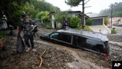 FILE - Residents evacuate past damaged vehicles after storms caused a mudslide, Feb. 5, 2024, in the Beverly Crest area of Los Angeles. The strongest storm of the year brought dangerous debris flows and slides across Southern California on Feb. 14, 2025.