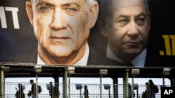 People walk on a bridge under an election campaign billboard of Blue and White party shows its party leader Benny Gantz, and Israeli Prime Minister Benjamin Netanyahu, in Ramat Gan, Israel, Feb. 18, 2020.