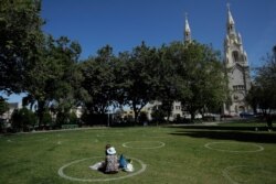 FILE - A woman and child sit in a circle designed to help prevent the spread of the coronavirus by encouraging social distancing at Washington Square park in front of Saints Peter and Paul Church in San Francisco, May 23, 2020.