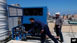 In this April 30, 2020 photo, Palestinian engineer Raed Nakhal from Palestine Children Relief Fund, right, and engineer Abdullah Dewik, check the GEN-M machine that generates safe drinking water from air around the roof of al-Rantisi pediatric hospital in