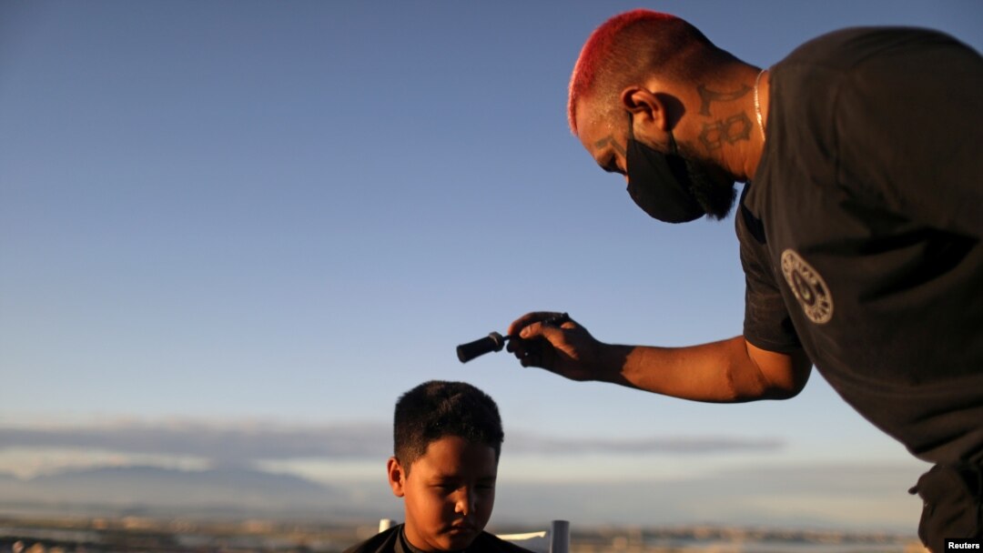 El barbero Renan Estate corta el pelo a un niño en su hogar como parte de su servicio "Delivery Barber", ya que su tienda está cerrada debido al brote de COVID-19), en el barrio marginal Complexo do Alemao en Río de Janeiro, el 22 de junio de 2020.