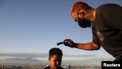 El barbero Renan Estate corta el pelo a un niño en su hogar como parte de su servicio "Delivery Barber", ya que su tienda está cerrada debido al brote de COVID-19), en el barrio marginal Complexo do Alemao en Río de Janeiro, el 22 de junio de 2020.