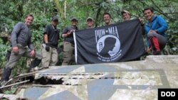 Anggota dari Defense POW / Badan Akuntansi MIA (DPAA), memegang bendera POW / MIA di atas sepotong puing logam dalam misi penyelidikan DPAA dekat desa Bhismaknagar, Arunachal Pradesh, India, 2 Desember 2016. (Foto: dok).