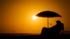 ARCHIVO - Una persona descansa bajo uns sombrilla de playa a la puesta del sol el 12 de septiembre de 2023 en Newport Beach, California, en uno de los veranos más calientes en la zona.