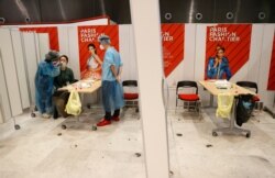 Health care workers wearing protective equipment gear collect a swab sample from a passenger at a COVID-19 screening booth set up in the arrival hall of Charles de Gaulle Airport, north of Paris, July 24, 2020.