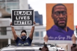 FILE - People hold up signs, including one with an image of George Floyd, outside the courthouse in Minneapolis, Minnesota, April 20, 2021, after former Minneapolis police officer Derek Chauvin was found guilty in the death of Floyd.