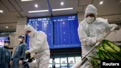 Workers wearing protective gear disinfect an arrival gate as an electronic board shows arrival information amid the coronavirus pandemic at the Incheon International Airport in Incheon, South Korea, Dec. 28, 2020.