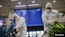 Workers wearing protective gear disinfect an arrival gate as an electronic board shows arrival information amid the coronavirus pandemic at the Incheon International Airport in Incheon, South Korea, Dec. 28, 2020.