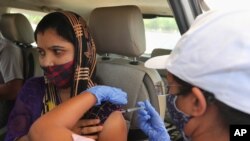 A woman receives a dose of Covishield, the Oxford-AstraZeneca vaccine for COVID-19 in her car at a drive-in vaccination facility in Ahmedabad, India, May 28, 2021.