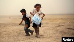 A girl, who fled from the violence in Mosul, carries a case of water at a camp on the outskirts of Arbil in Iraq's Kurdistan region, June 12, 2014.