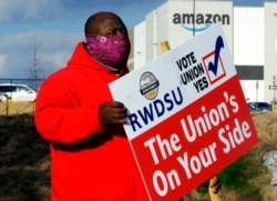 FILE - Michael Foster of the Retail, Wholesale and Department Store Union holds a sign outside an Amazon facility in Bessemer, Ala., where labor is trying to organize workers, Feb. 9, 2021.