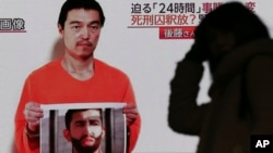 FILE - A passerby is silhouetted against a large TV broadcasting a news program showing a still photo of Japanese hostage Kenji Goto holding what appears to be a photo of Jordanian pilot Mu'ath al-Kaseasbeh, in Tokyo, Jan. 28, 2015.