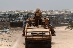 FILE - Kenya Defence Force (KDF) soldiers, serving in the African Union Mission in Somalia (AMISOM), patrol past stockpiles of charcoal near the Kismayo sea port town in lower Juba region, Somalia, Feb. 27, 2013.