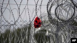 FILE - A punctured ball hangs on barbed wire in the heavily guarded camp at Serbia's border with Hungary, near the Horgos border crossing, Serbia, Sept. 19, 2017. 