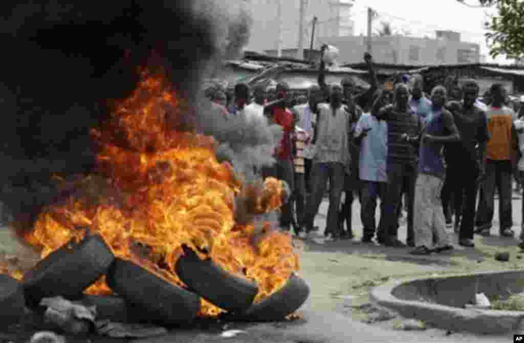 Supporters of opposition candidate Alassane Ouattara shout 'We don't want Gbagbo,' as they stand beside a street fire set in protest at incumbent President Laurent Gbagbo remaining in office, in the Koumassi neighborhood of Abidjan, Ivory Coast, 06 Dec 20