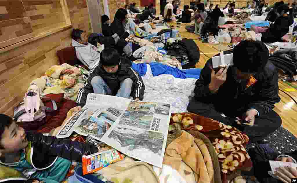 A young boy (C) reads a newspaper reporting on the earthquake at a shelter for evacuees in the town of Minamisoma in Fukushima Prefecture a day after an 8.9 magnitude quake and tsunami devastated the region, March 12, 2011. (AFP)