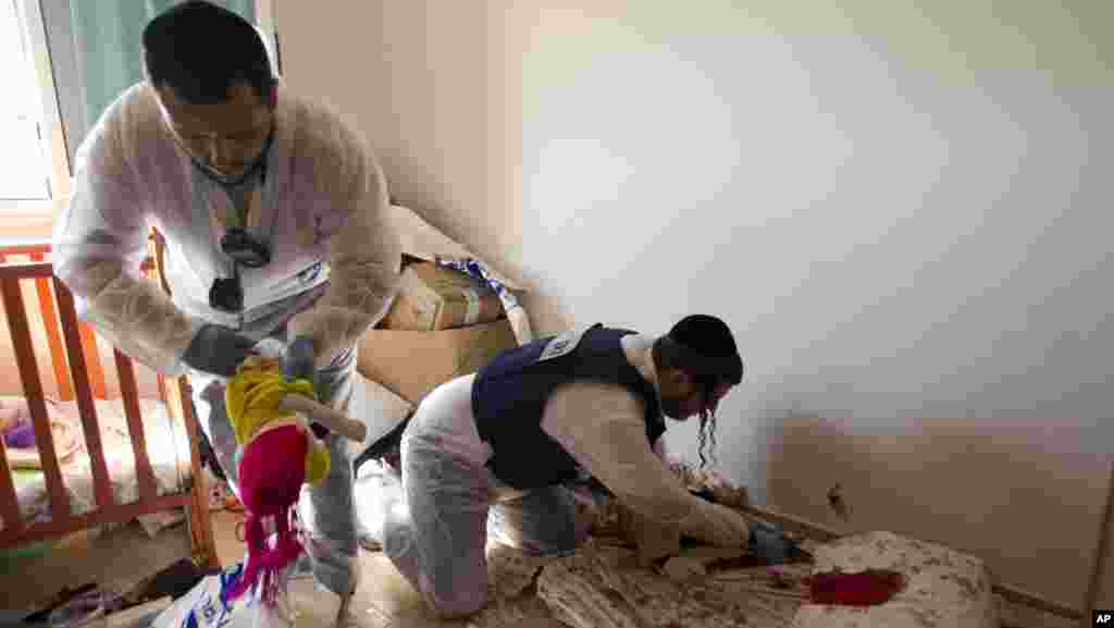 Zaka volunteers clean blood stains from a pillow and a baby toy in a children's room in apartment building that was hit by a rocket fired from the Gaza Strip, where three people were killed in Kiryat Malachi, southern Israel, Kiryat Malachi, southern Isra