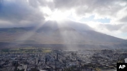 FILE - Rays of sunlight pierce through the clouds August 10, 2023, above homes burned by wildfires in Lahaina, Hawaii. Days later, a shocking claim spread on YouTube and TikTok: The blaze was set deliberately, using futuristic energy weapons developed by the U.S. military.