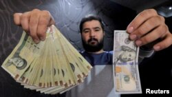 FILE - A money changer displays a U.S. $100 bill and the amount being given when converting it into Iranian rials at a currency exchange shop in Tehran's business district, Jan. 20, 2016. The rial hit record lows against the dollar in June 2018. 