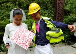 Henry Tong, wearing a helmet and a first aid vest associated with the anti-extradition bill protests, poses for pictures with his wife, Elaine To, after getting married in Hong Kong, Aug. 4, 2019. The placard reads,"Let's go for it together."
