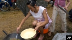 FILE - A child holds an umbrella as a Chinese woman tries to cook in the rain.