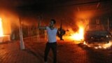 An armed man waves his rifle as buildings and cars are engulfed in flames after being set on fire inside the US consulate compound in Benghazi late on September 11, 2012. 