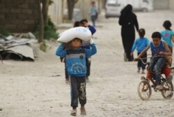 FILE - A boy carries food aid given by UN's World Food Program in Raqqa, Syria, April 26, 2018.