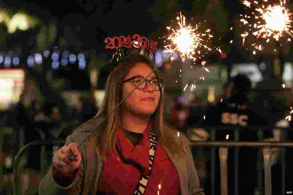 Uma mulher segura um foguete durante o concerto do músico, cantor e político panamiano Ruben Blades no monumento Angel de la Independencia durante a celebração do Ano Novo de 2024 na Cidade do México, a 31 de dezembro de 2023.