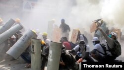 Manifestantes se ponen a cubierto mientras chocan con agentes de la policía antidisturbios durante una protesta contra el golpe militar en Rangún, Myanmar, el 28 de febrero de 2021.