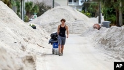 David DeMeza camina con sus pertenencias entre calles cubiertas de arena arrastrada por el huracán Helene, el 2 de octubre de 2024, en Treasure Island, Florida.