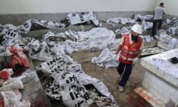 FILE - A rescue worker walks past covered bodies, killed during a fire at a garment factory, after they were brought to the Jinnah hospital morgue in Karachi, Sept. 12, 2012.
