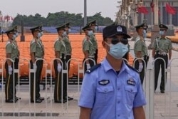 A police officer wearing a face mask to help curb the spread of the coronavirus stands guard near masked Chinese paramilitary officers preparing for their duties near rows of seats setup on Tiananmen Square in Beijing, June 28, 2021.