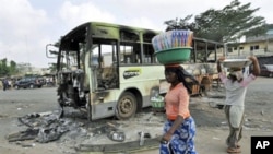 Des femmes passant devant l'épave d'un autobus incendié au quartier pro-Ouattara d'Abobo, à Abidjan