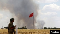 FILE - A Turkish soldier stands guard while smoke rises in the Syrian town of Kobani as it is seen from the Turkish border town of Suruc in Sanliurfa province, Turkey, June 26, 2015. 