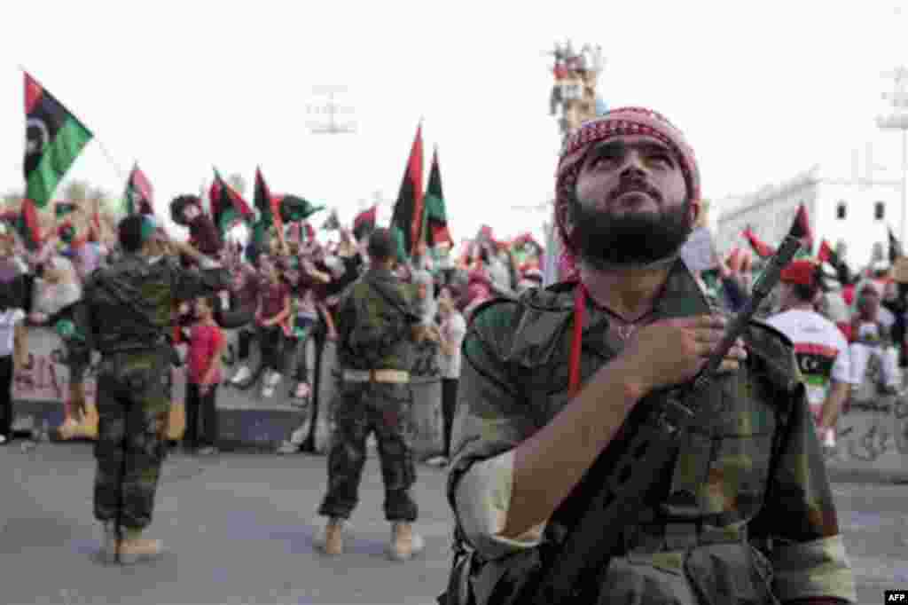 A rebel fighter, on guard duty during a women's demonstration, puts his hand on his heart while listening to the new national anthem in the former Green Square, now called Martyrs' Square in Tripoli, Libya, Friday, Sept. 2, 2011. Rebel fighters pushed clo