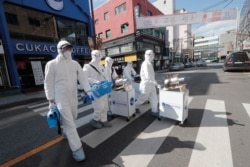 Workers wearing protective gear arrive to spray disinfectant as a precaution against the new coronavirus at a shopping street in Seoul, South Korea, Feb. 27, 2020.