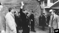 President Ronald Reagan waves just before he is shot outside the Washington Hilton on Monday, March 30, 1981. From left are secret service agent Jerry Parr, in raincoat, who pushed Reagan into the limousine; press secretary James Brady, who was seriously 