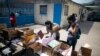 Una maestra revisa una lista de estudiantes y tiene tareas traídas por los padres de los estudiantes que no tienen internet en casa, en la escuela "Fe y Alegría", en el barrio Las Mayas de Caracas, Venezuela. Mayo 12, 2020. Foto: AP.