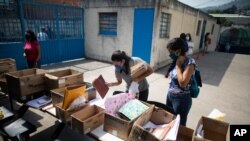 Una maestra revisa una lista de estudiantes y tiene tareas traídas por los padres de los estudiantes que no tienen internet en casa, en la escuela "Fe y Alegría", en el barrio Las Mayas de Caracas, Venezuela. Mayo 12, 2020. Foto: AP.