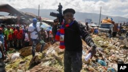 FILE - Jimmy Cherizier, also known as Barbecue, the leader of the "G9 and Family" gang, stands next to a garbage pile to call attention to the conditions people live in as he leads a march against kidnapping through La Saline neighborhood in Port-au-Prince, on October 22, 2021. 