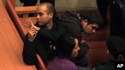 Juan Flores, left, waves to an unidentified person in the back of the courtroom as he sits handcuffed alongside fellow suspects Guillermo Duran, top right, and Nataly Casanova during their hearing in Santiago, Chile, Sept. 23, 2014.