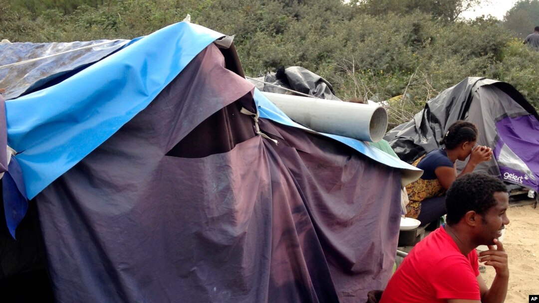 FILE - People sit by a tent at a makeshift camp in Calais, northern France, Sept. 7, 2014.