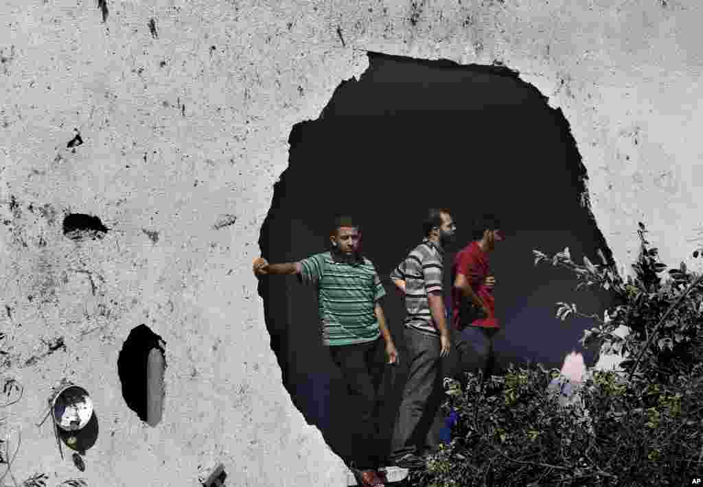 Palestinians standing next to a damaged wall watch rescuers searching for bodies and survivors under the rubble of an apartment building that was destroyed by an Israeli missile strike, in Gaza City,&nbsp; July 21, 2014.