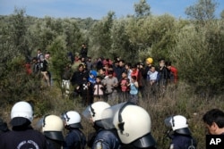 FILE - Police block a road as migrants look on during clashes outside the Moria refugee camp on the northeastern Aegean island of Lesbos, Greece, March 2, 2020.